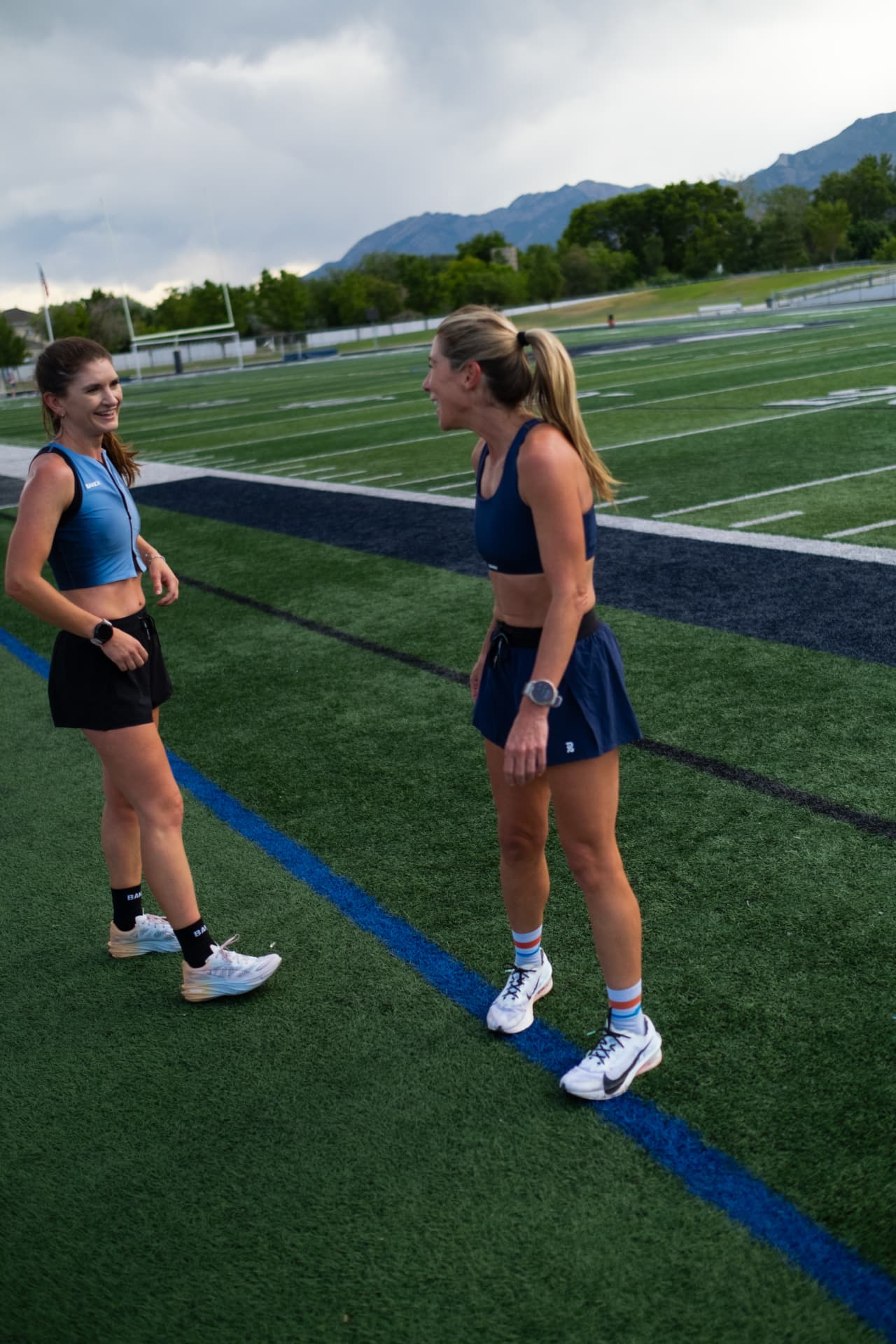 Two runners laughing on the track after a session, mountains behind them