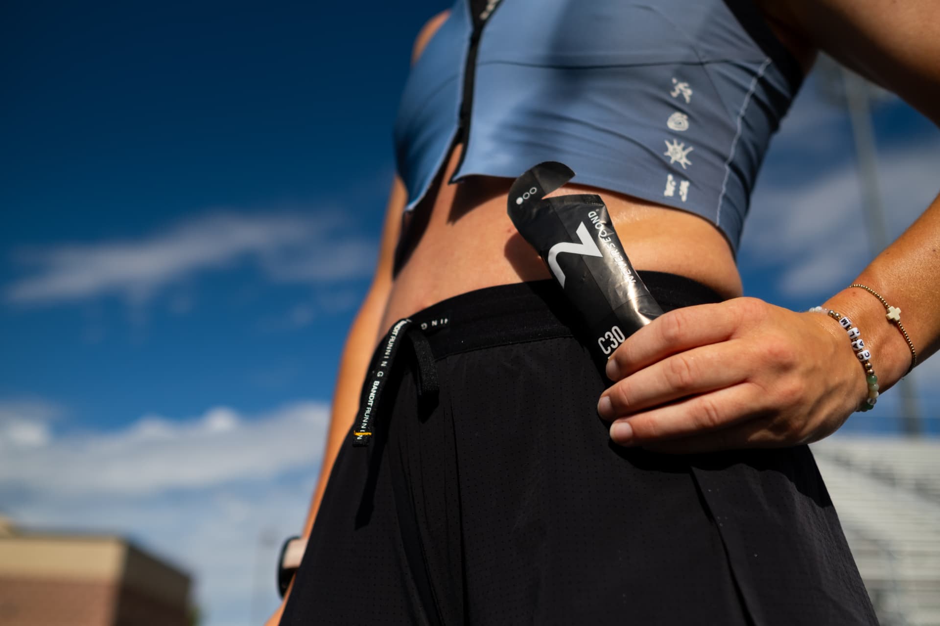 Runner pulling a fueling gel from her shorts pocket against a blue sky